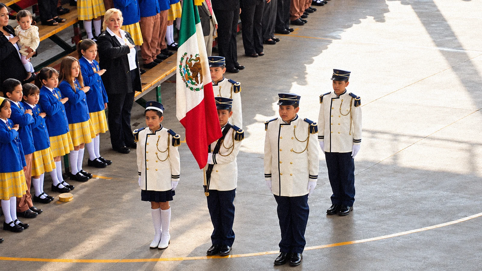 Estudiantes con uniforme participan en una ceremonia con la bandera de México.